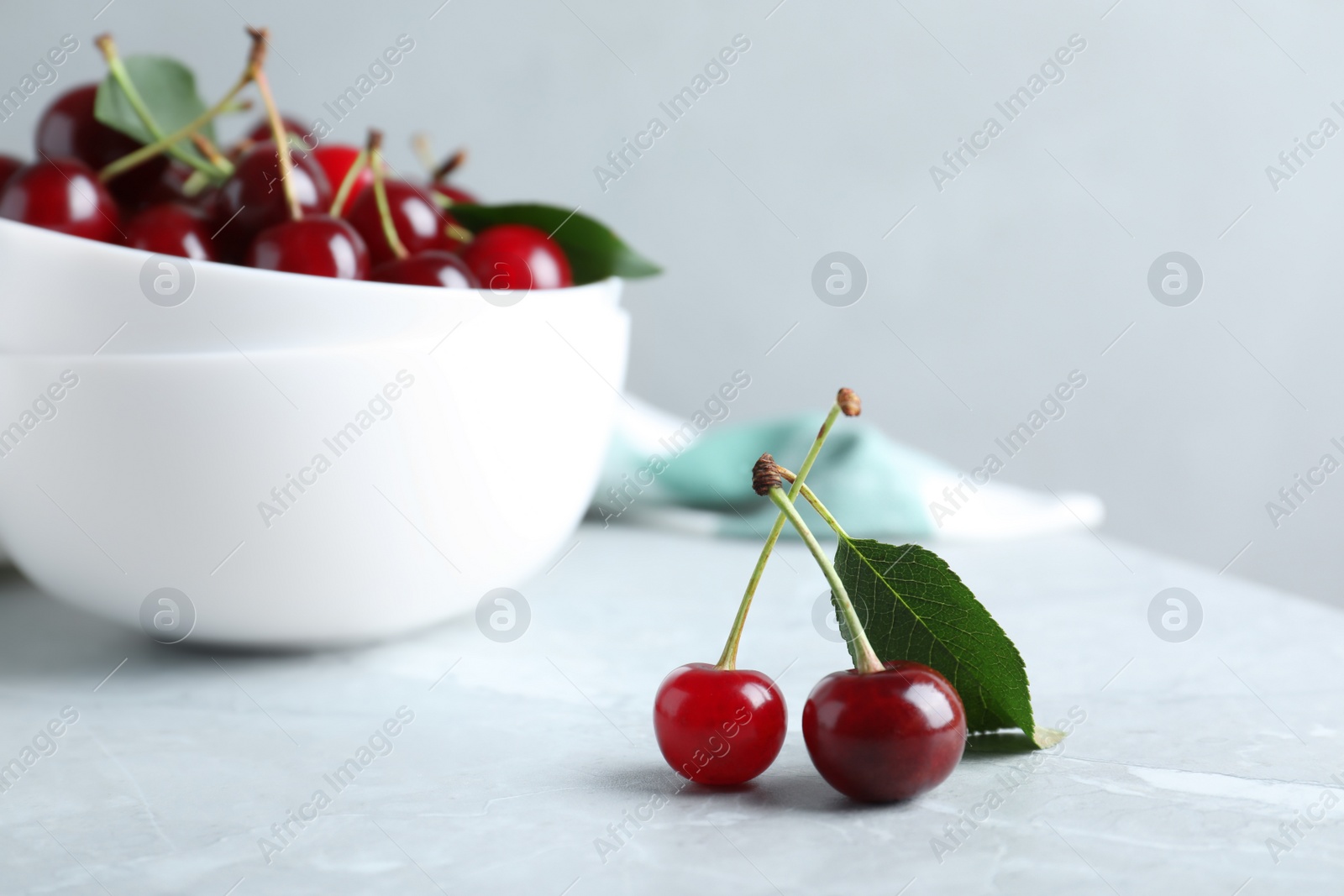 Photo of Sweet juicy cherries with leaves on grey marble table, closeup