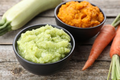 Photo of Tasty puree in bowls, zucchini and carrots on wooden table, closeup