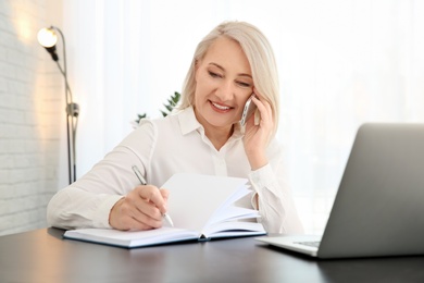 Photo of Mature woman talking on mobile phone at workplace