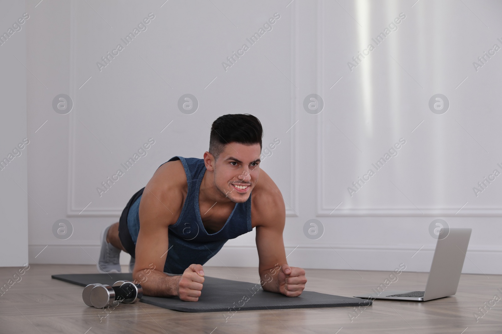 Photo of Handsome man doing plank exercise on yoga mat while watching online class indoors