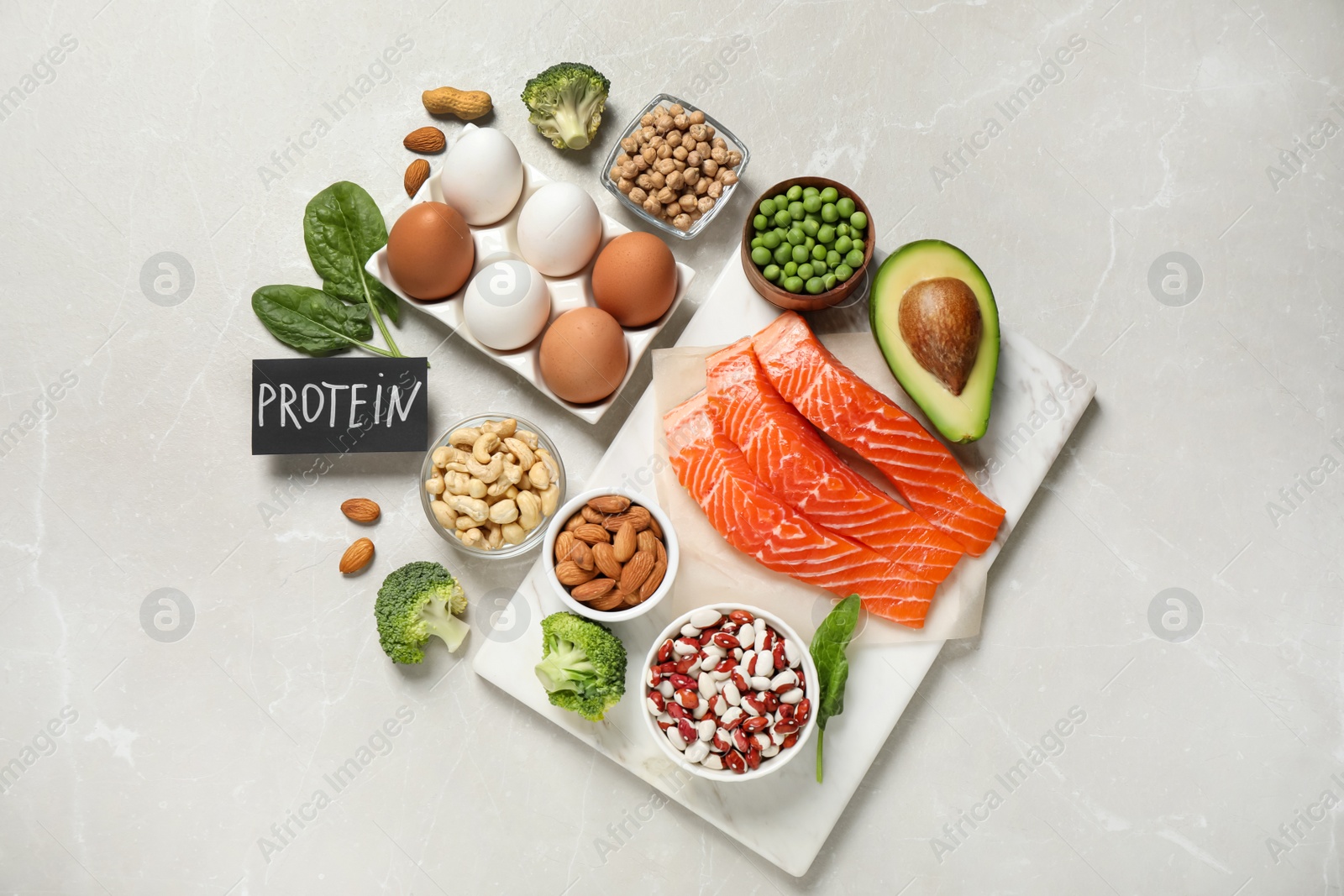 Photo of Card with word PROTEIN and different products on light marble table, flat lay