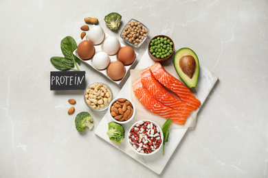 Photo of Card with word PROTEIN and different products on light marble table, flat lay