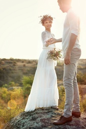 Happy newlyweds with beautiful field bouquet outdoors