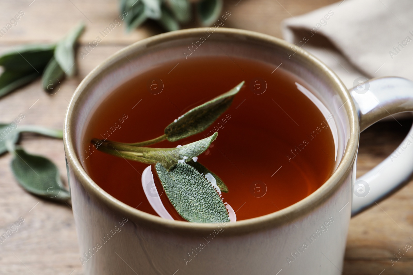 Photo of Cup of aromatic sage tea with fresh leaves on wooden table, closeup