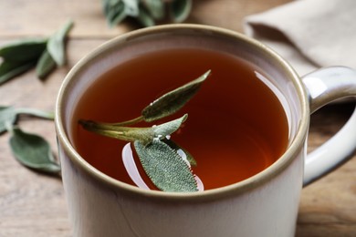 Photo of Cup of aromatic sage tea with fresh leaves on wooden table, closeup