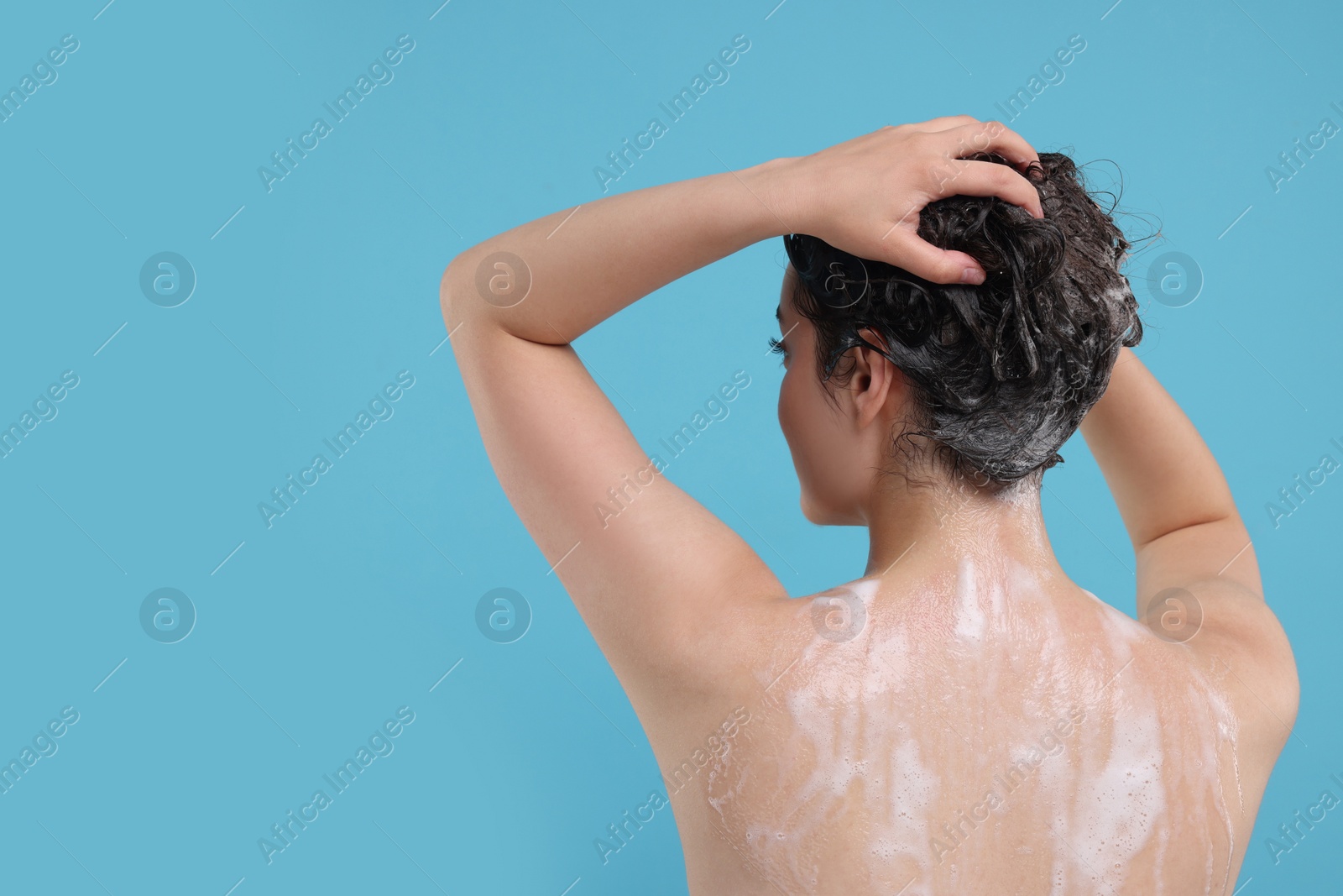Photo of Woman washing hair on light blue background, back view. Space for text
