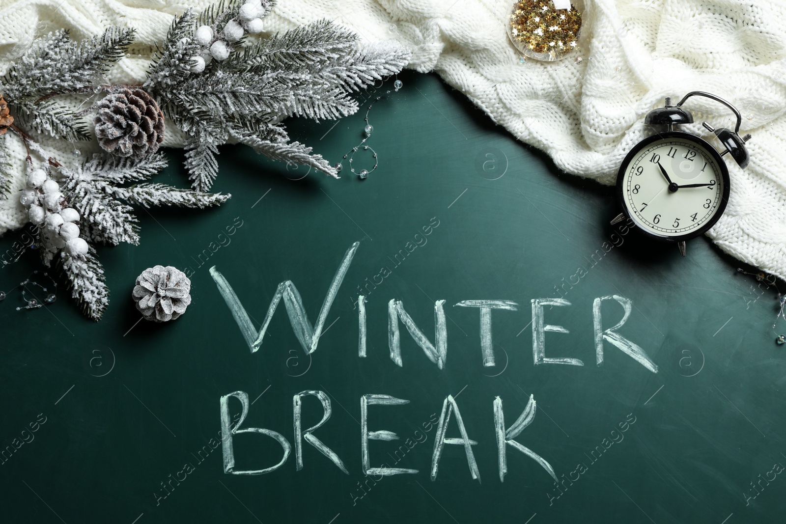 Photo of Flat lay composition of Christmas decorations, knitted plaid and alarm clock on school blackboard with phrase Winter Break