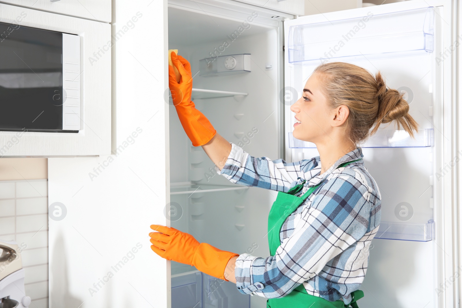 Photo of Woman in rubber gloves cleaning empty refrigerator at home