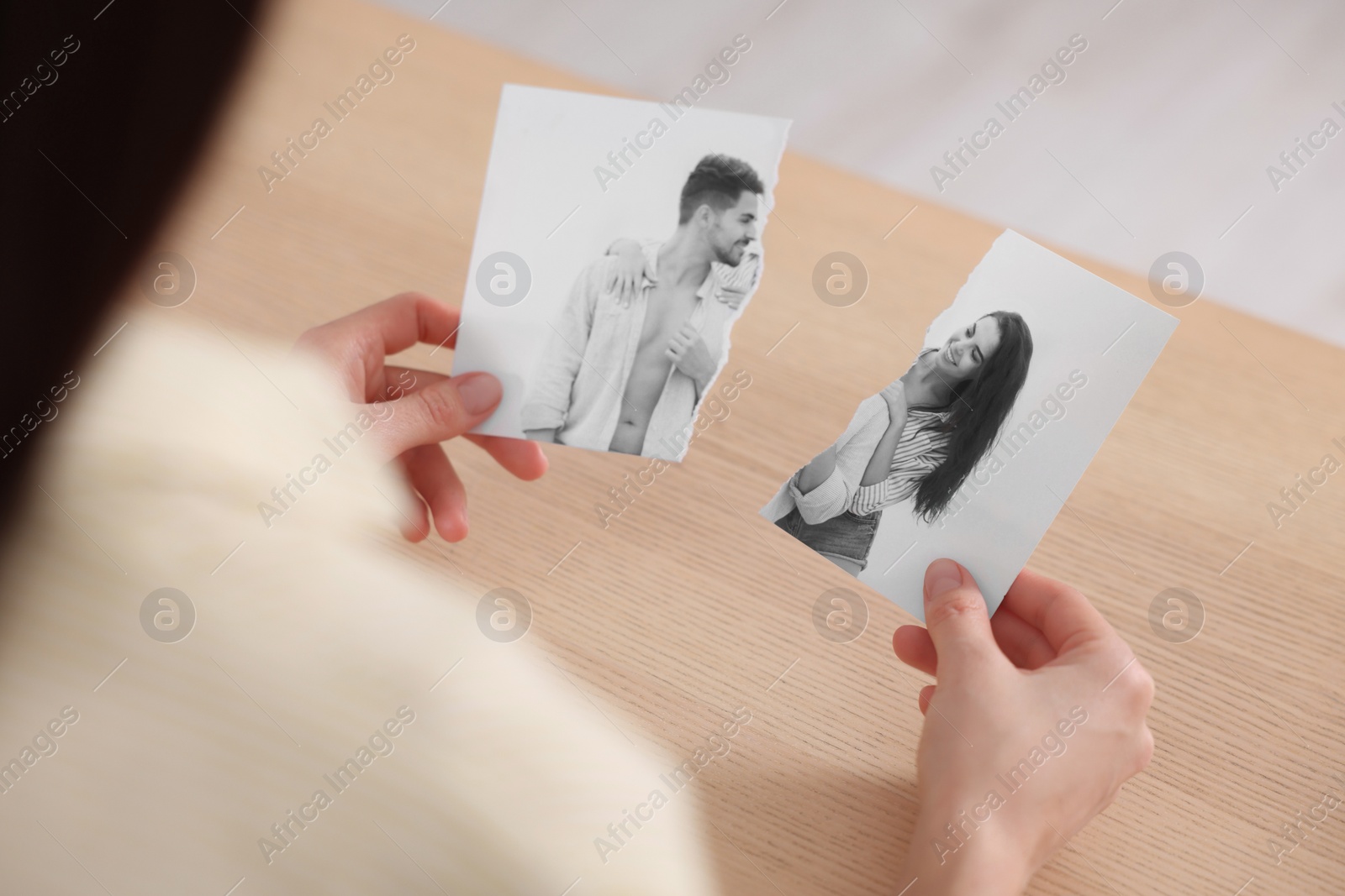 Image of Divorce and breakup. Woman holding parts of ripped black and white photo at table, closeup