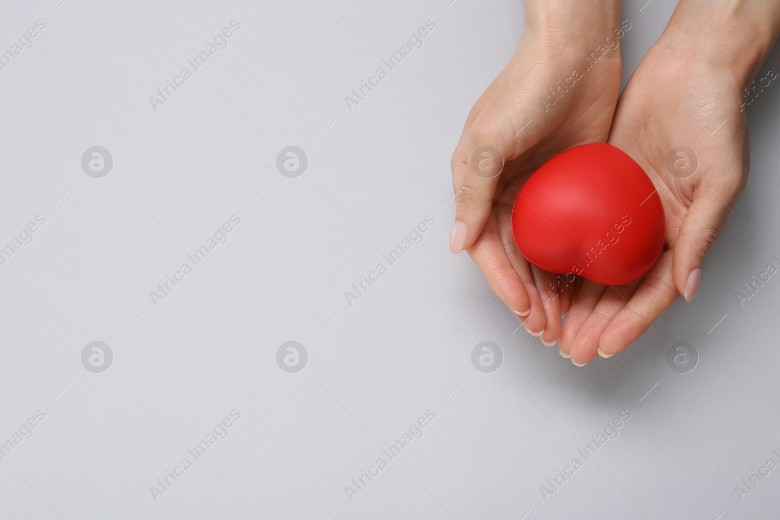 Photo of Woman holding red decorative heart on grey background, top view and space for text. Cardiology concept