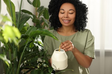 Photo of Happy woman watering beautiful potted houseplants indoors