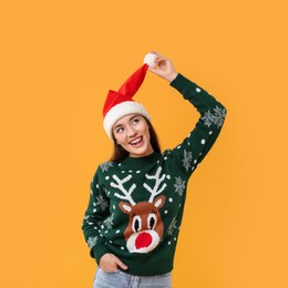 Photo of Happy young woman in Christmas sweater and Santa hat on orange background