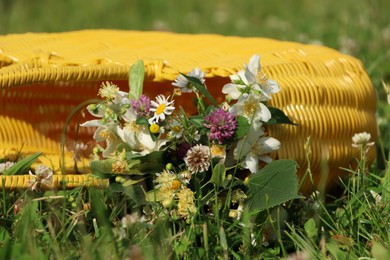 Photo of Yellow wicker bag with different wildflowers and herbs in meadow on sunny day, closeup