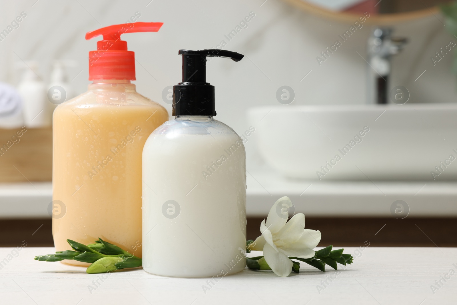Photo of Dispensers of liquid soap and freesia flower on white table in bathroom, space for text