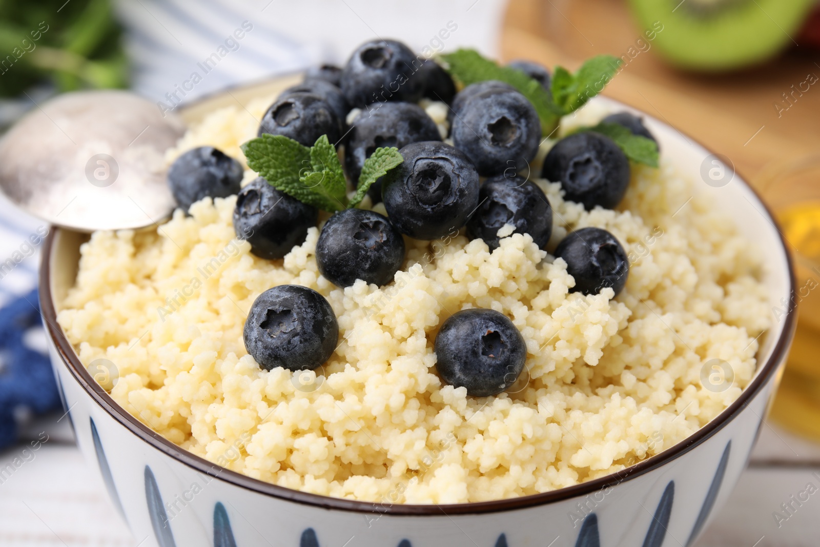 Photo of Bowl of tasty couscous with blueberries and mint on table, closeup