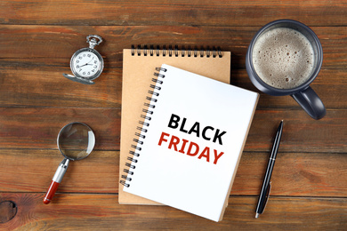 Image of Notebook with text BLACK FRIDAY, cup of coffee and magnifying glass on wooden table, flat lay