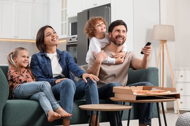 Photo of Happy family watching TV with pizza on sofa at home