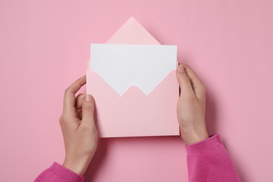 Photo of Woman holding letter envelope with card at pink table, top view