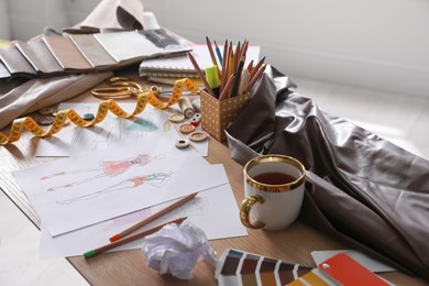 Sketches of clothes and different stuff on wooden table indoors. Fashion designer's workplace