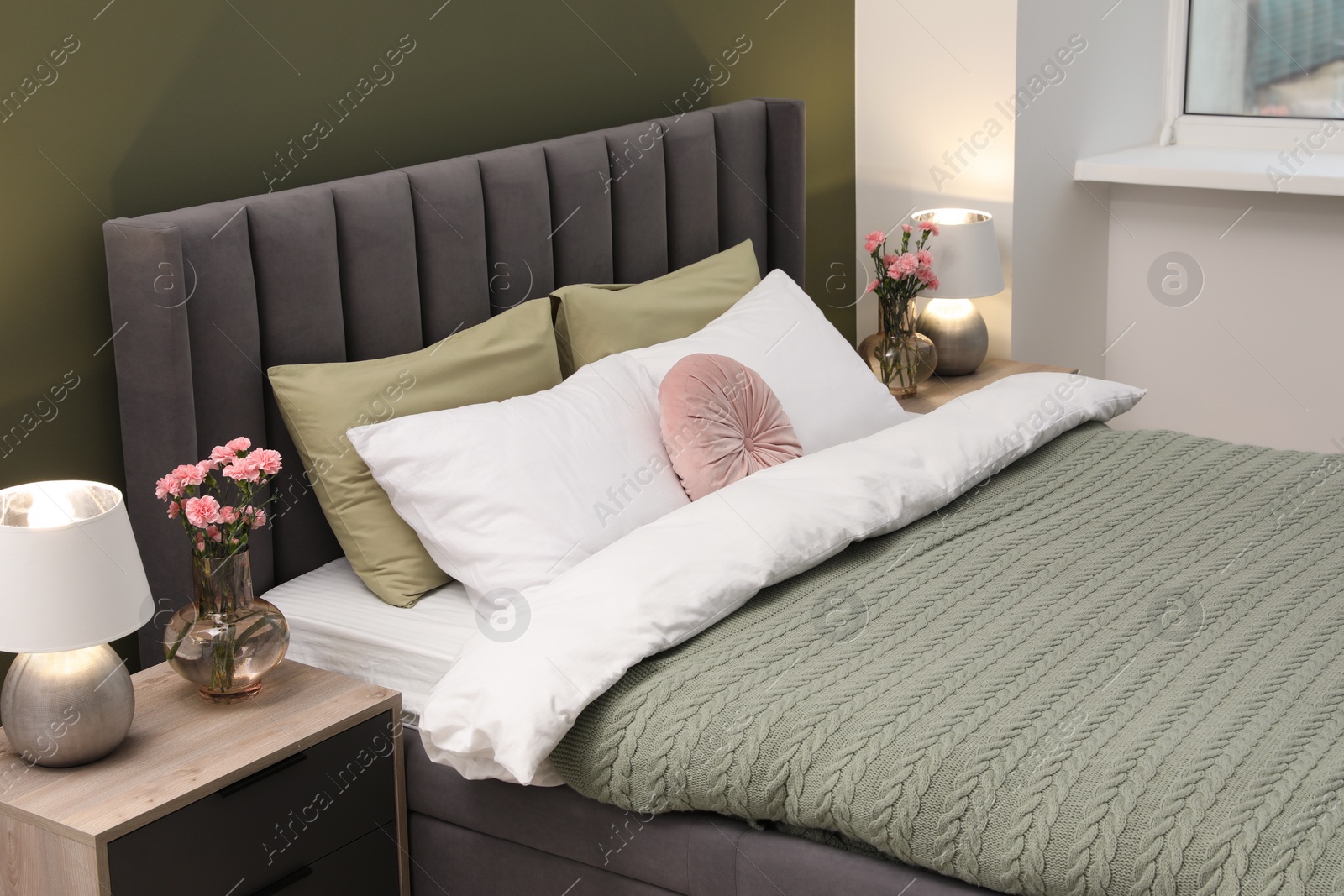 Photo of Large comfortable bed, lamps and beautiful flowers in stylish room. Interior design