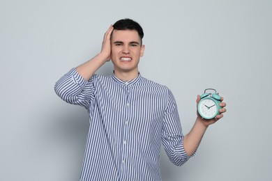 Emotional young man with alarm clock on light grey background. Being late concept