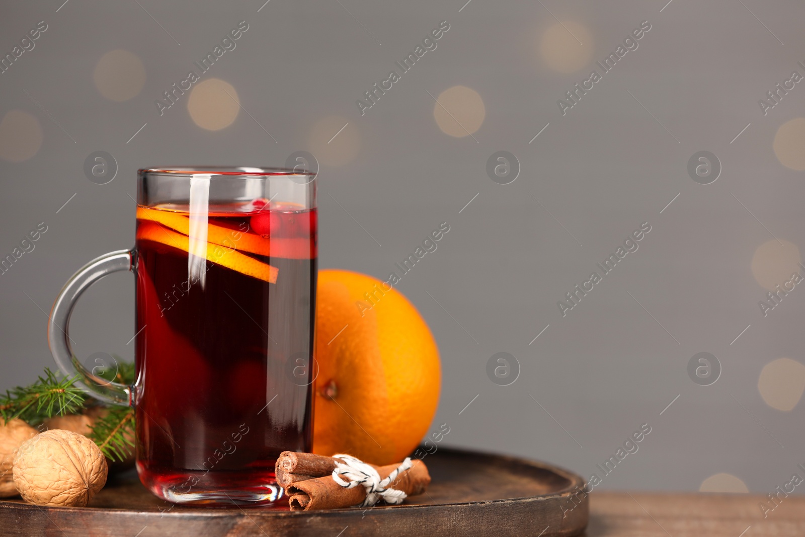 Photo of Aromatic mulled wine in glass cup on table against grey background with blurred lights, closeup. Space for text