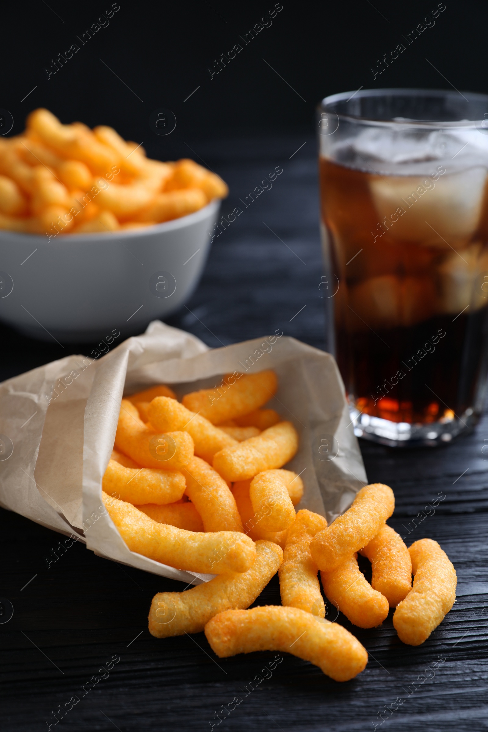 Photo of Crunchy cheesy corn snack on black wooden table, closeup