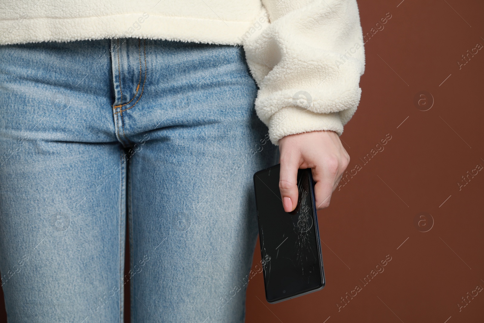 Photo of Woman holding damaged smartphone on brown background, closeup. Device repairing