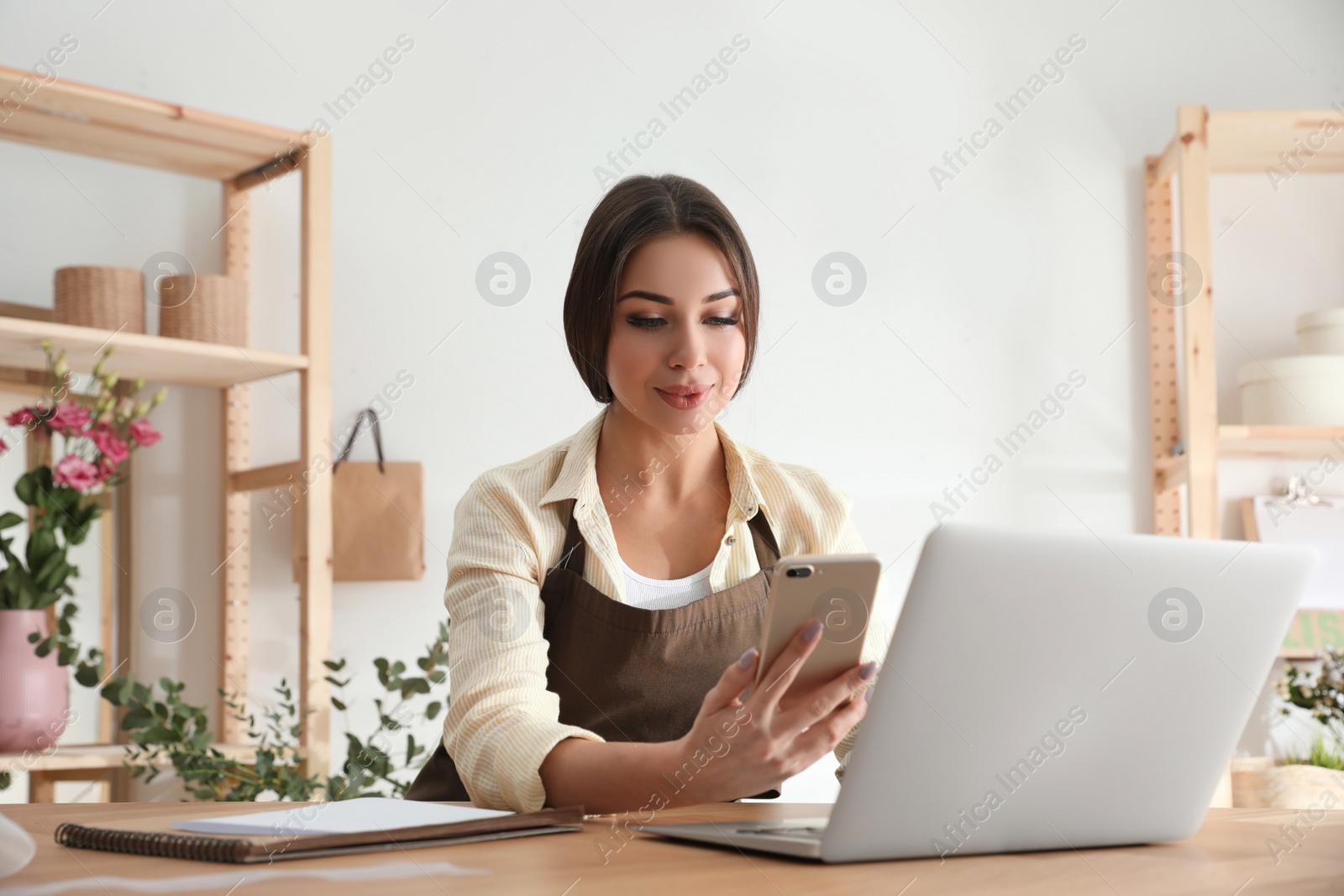 Photo of Florist with smartphone and laptop in workshop