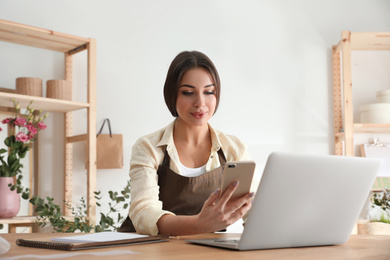 Florist with smartphone and laptop in workshop