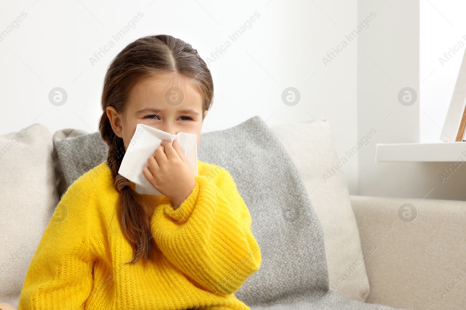 Photo of Girl blowing nose in tissue on sofa in room. Cold symptoms