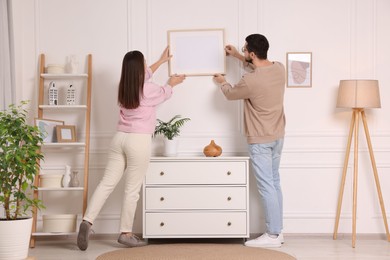 Photo of Man and woman hanging picture frame on white wall at home