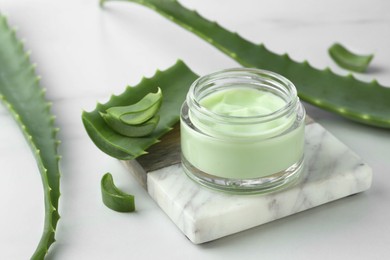 Photo of Jar with cream and cut aloe leaves on white table, closeup