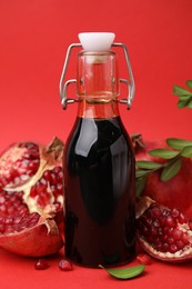 Photo of Tasty pomegranate sauce in bottle, branches and fruits on red background, closeup