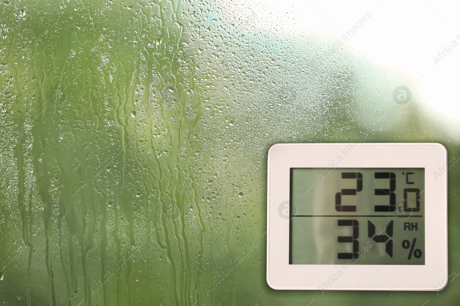 Image of Digital hygrometer with thermometer on glass with water drops. Space for text