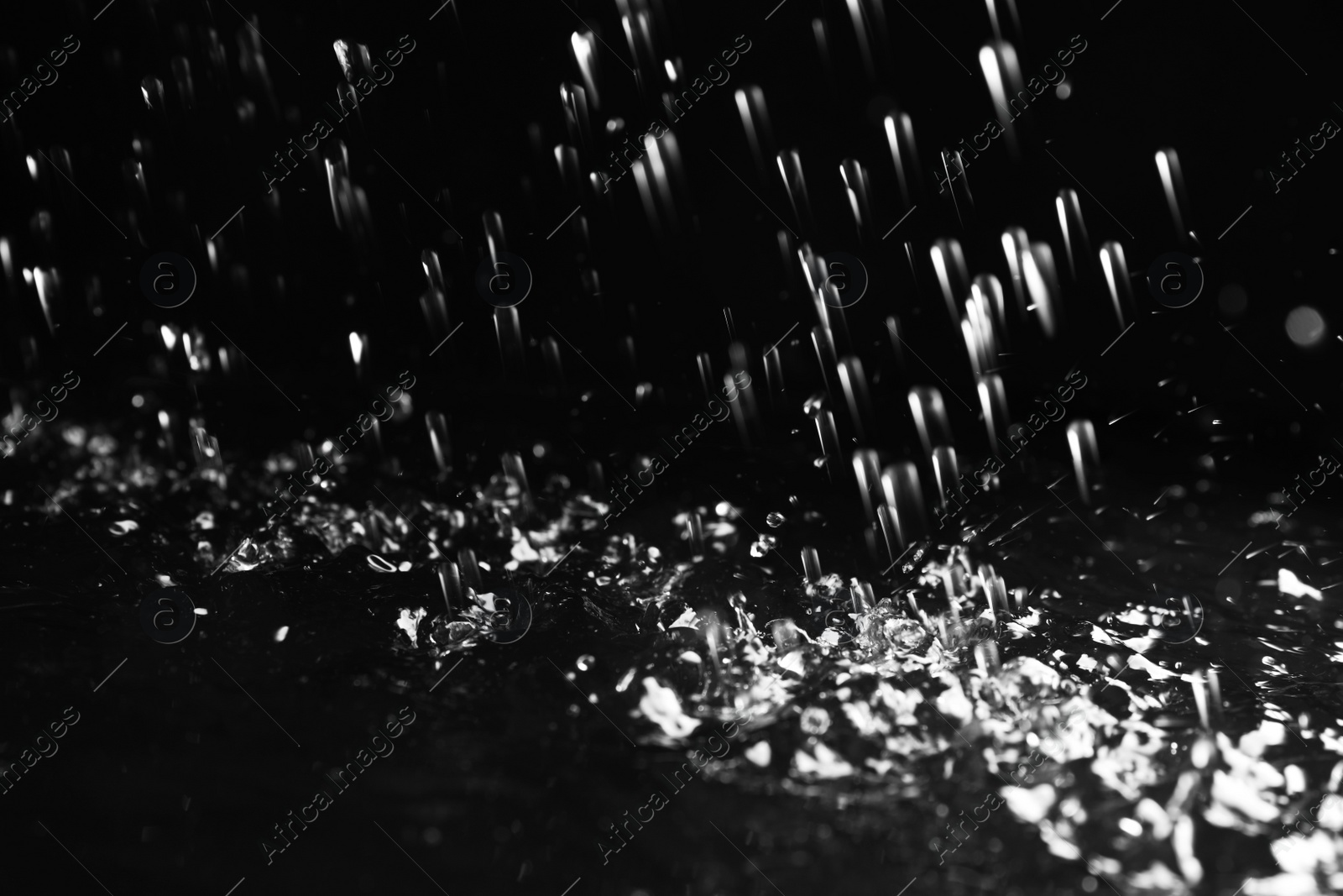 Photo of Heavy rain falling down on ground against dark background, closeup