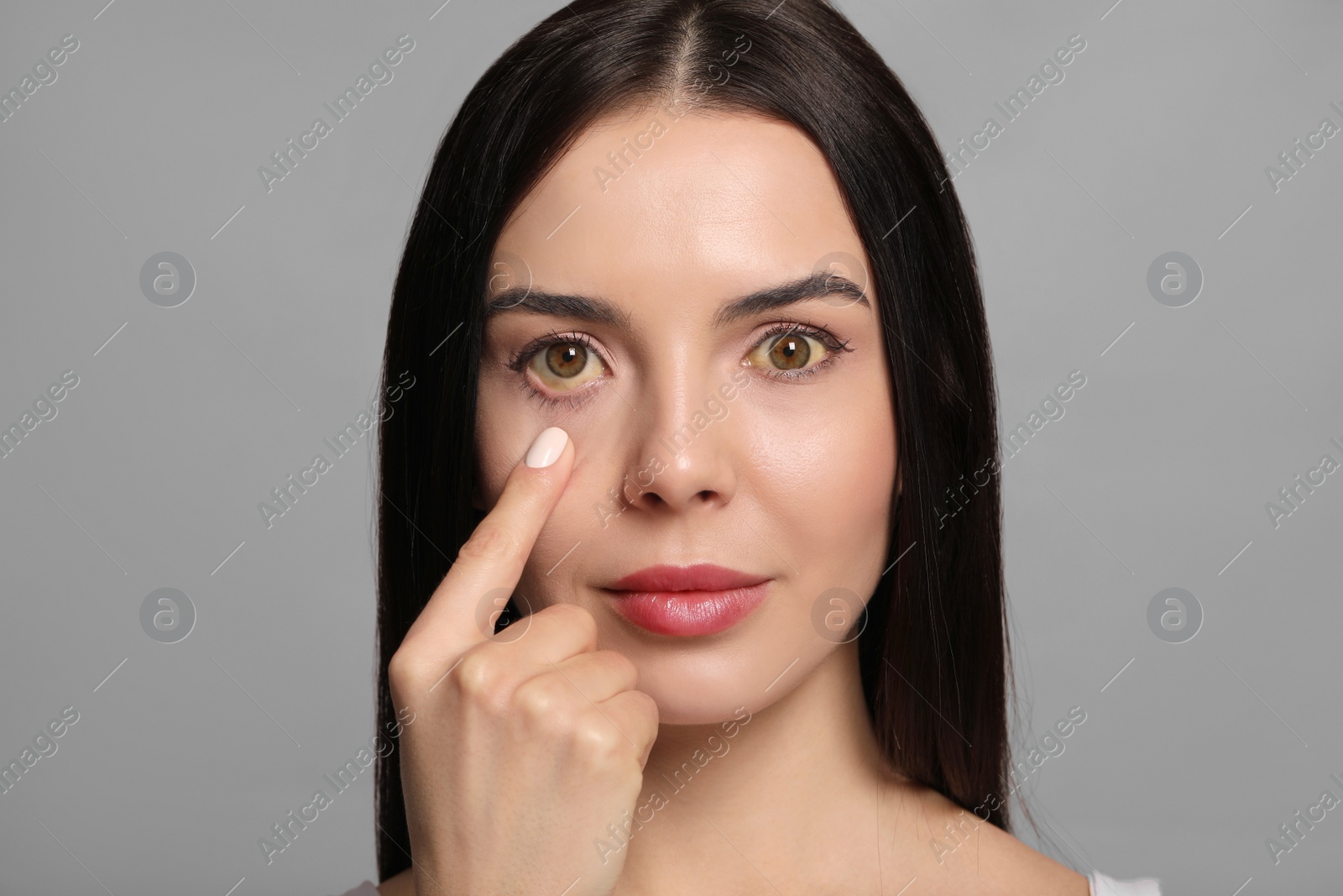 Photo of Woman checking her health condition on grey background. Yellow eyes as symptom of problems with liver