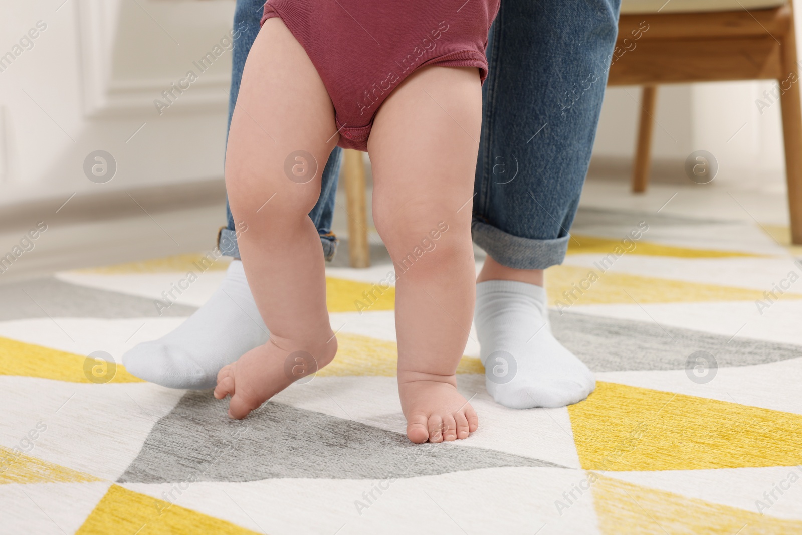 Photo of Mother supporting her baby son while he learning to walk on carpet at home, closeup