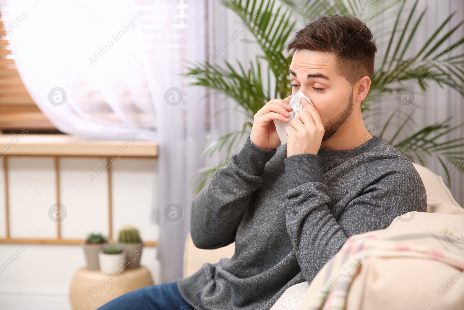 Photo of Sick young man sneezing at home. Influenza virus