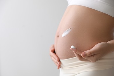 Photo of Young pregnant woman with cosmetic product on belly against grey background, closeup. Space for text