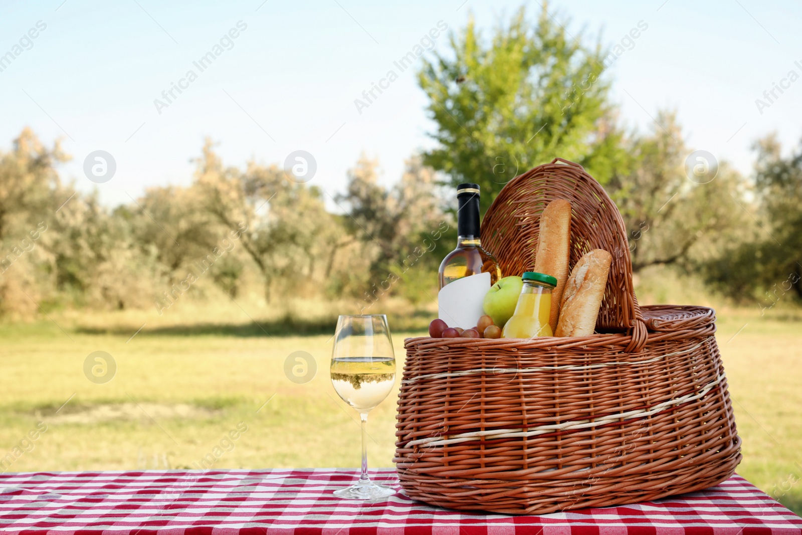 Photo of Wicker picnic basket with wine and snacks on table in park. Space for text