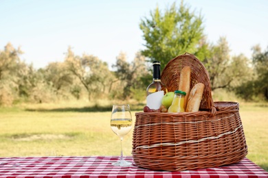 Wicker picnic basket with wine and snacks on table in park. Space for text