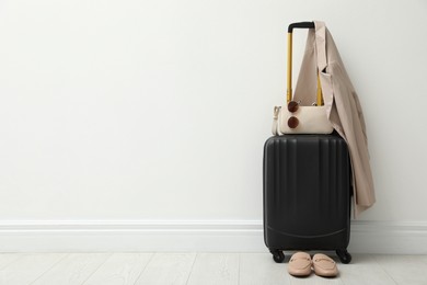 Photo of Packed suitcase, shoes, jacket and accessories near white wall indoors. Space for text