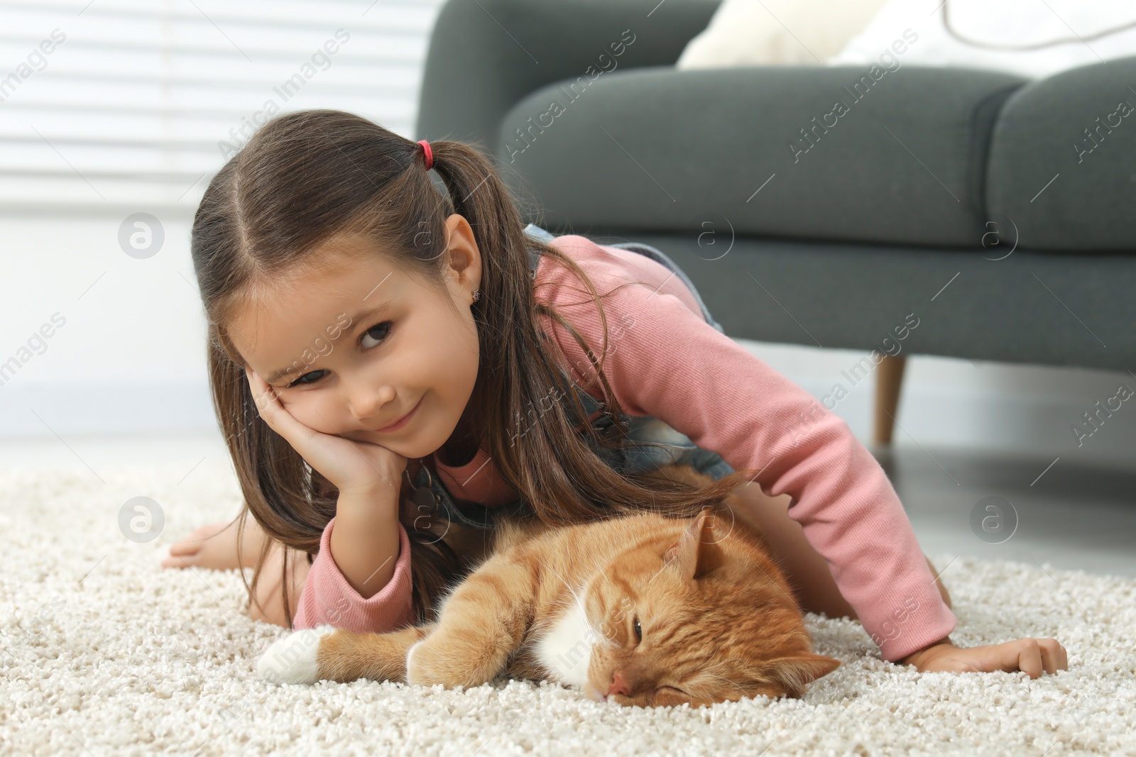 Photo of Smiling little girl and cute ginger cat on carpet at home