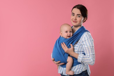 Photo of Mother holding her child in sling (baby carrier) on pink background. Space for text
