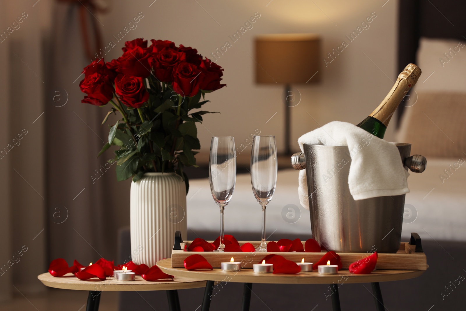 Photo of Honeymoon. Sparkling wine, glasses and bouquet of roses on wooden table in room