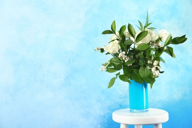 Vase with bouquet of beautiful flowers on table against color background. Space for text