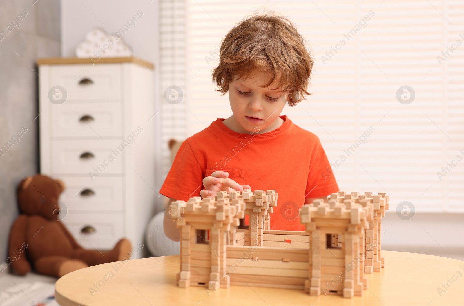 Photo of Cute little boy playing with wooden fortress at table in room. Child's toy