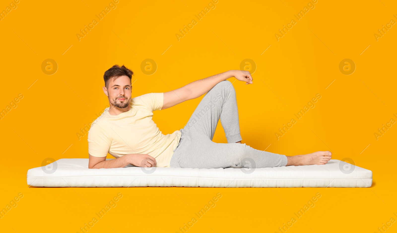 Photo of Man lying on soft mattress against orange background