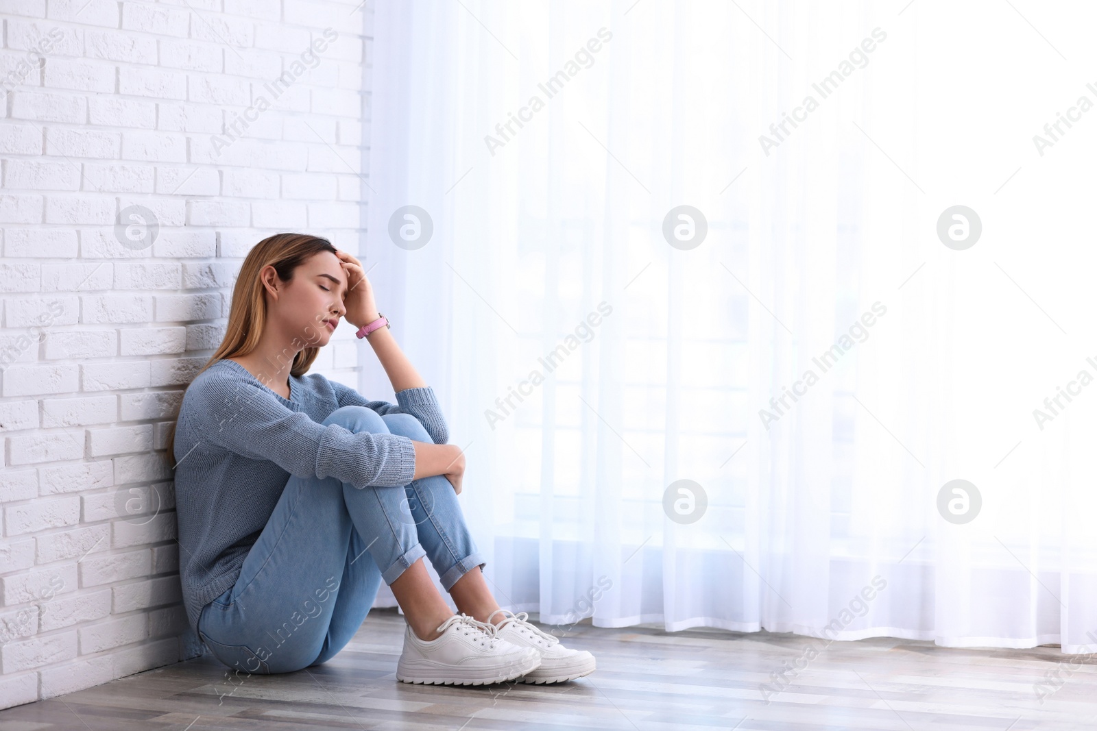 Photo of Emotional teenage girl sitting on floor indoors. Space for text